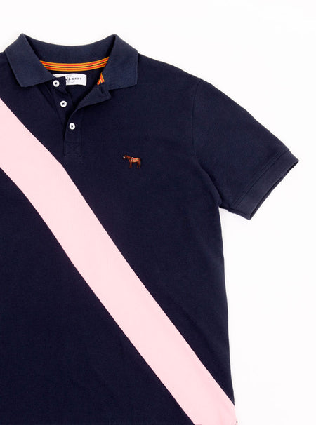 Flat lay of men's navy 100% cotton polo shirt with pale pink sash detail and Newmarket 875 horse logo embroidered on the front.